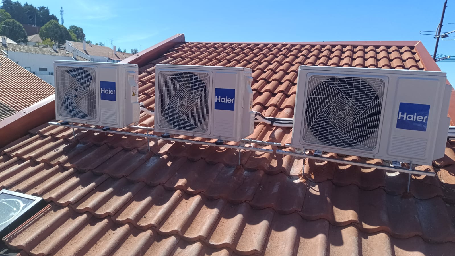 Três unidades exteriores Haier montadas numa estrutura de suporte sobre uma cobertura de telha